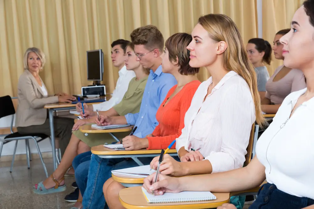 Studenti di liceo e allievi in un'aula scolastica seguono una lezione prendendo appunti sui quaderni.