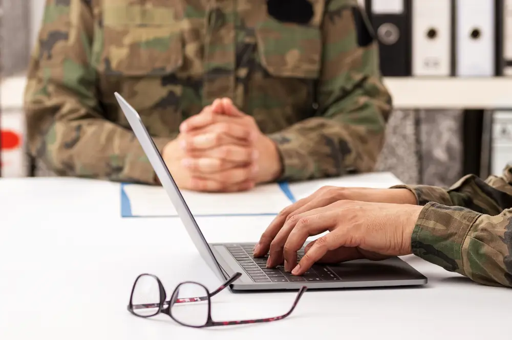 Militari in divisa mimetica durante le procedure di selezione e reclutamento in caserma, con un soldato al computer.