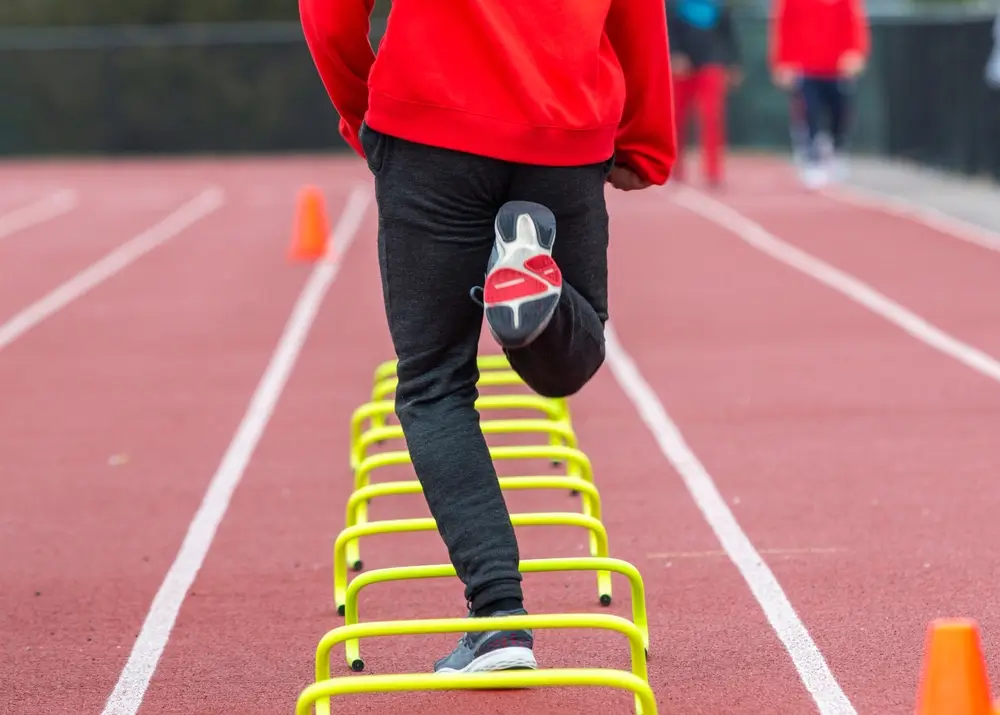 Candidato che supera piccoli ostacoli sulla pista di atletica durante le prove di efficienza fisica per l'Esercito.