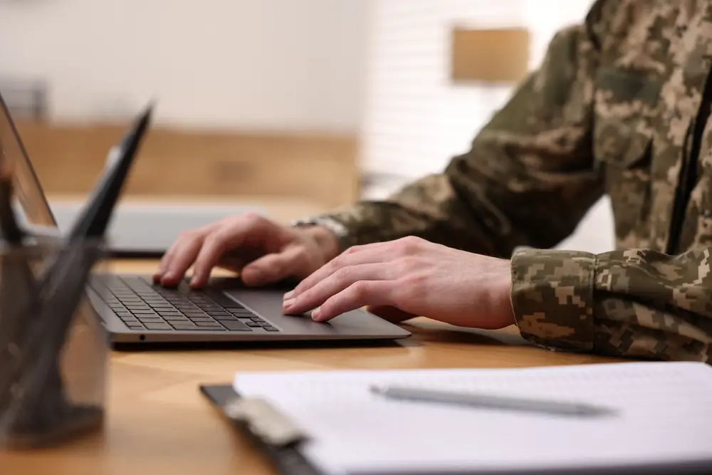 Cadetto militare in divisa mimetica mentre studia al computer portatile per la sua formazione da ufficiale.