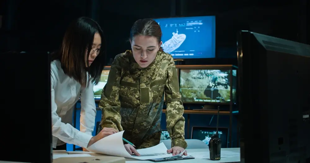 Una donna soldato in divisa mimetica analizza documenti durante un'esercitazione di addestramento militare.