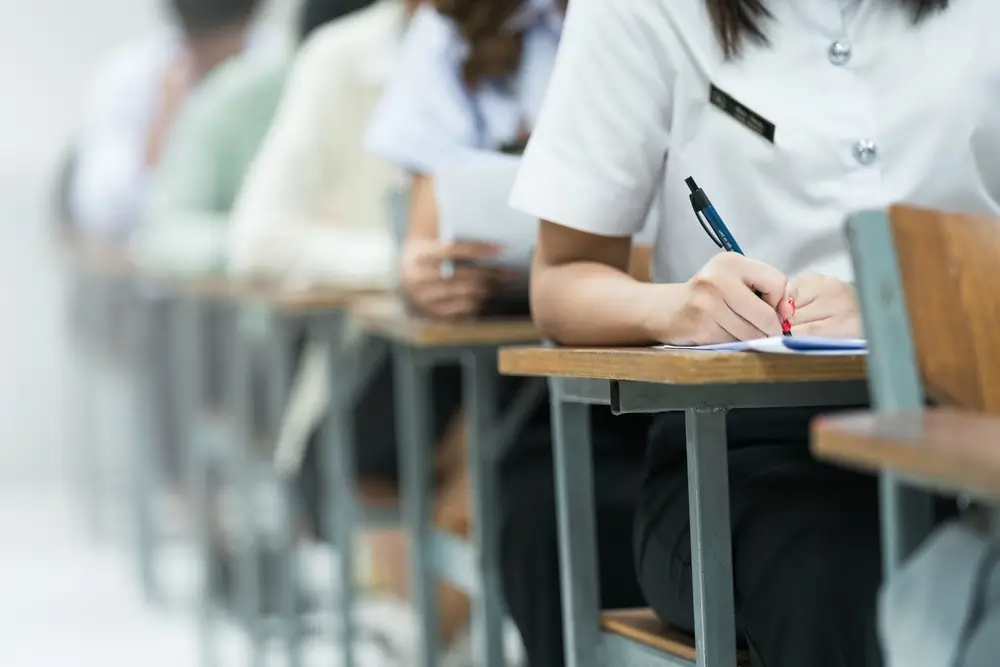 Studenti impegnati in una prova d'esame scritta in un'aula universitaria durante un concorso pubblico.