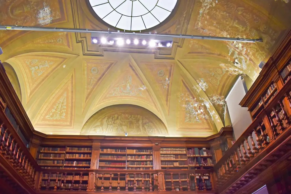 Interno della biblioteca storica dell'Accademia Militare con scaffali in legno e soffitto a volta affrescato.