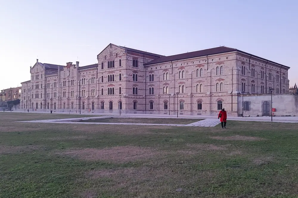 Maestoso edificio storico della scuola militare con facciata in pietra e mattoni rossi davanti a un grande prato.