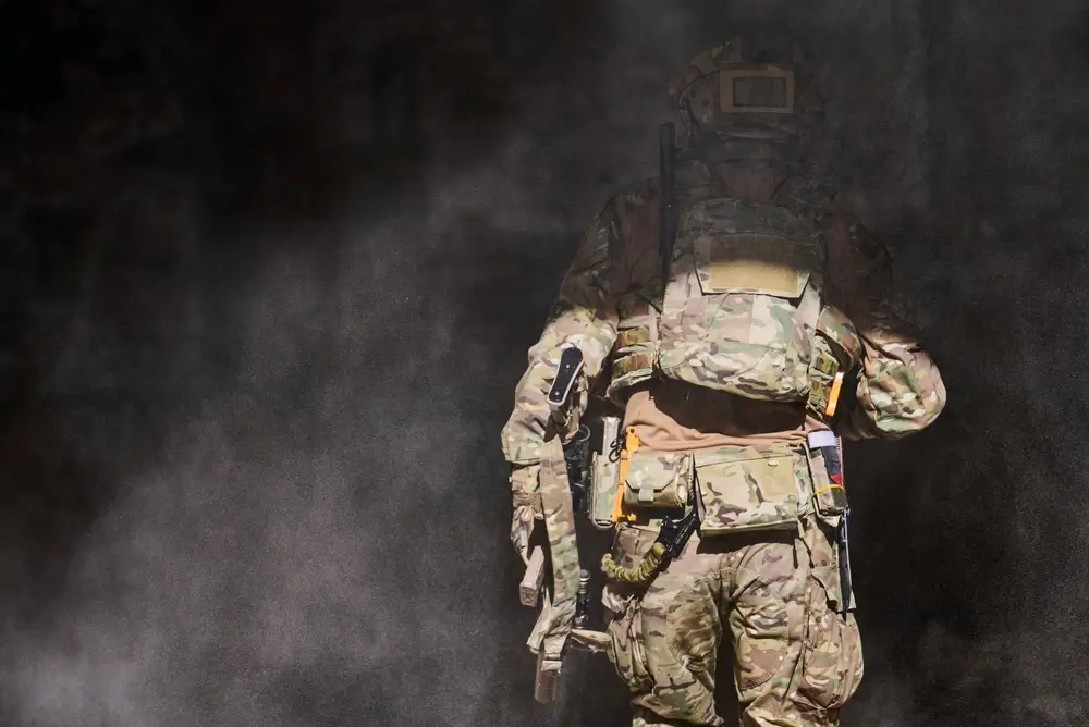 Ufficiale dell'Esercito in divisa militare durante un addestramento tattico in assetto operativo tra fumo e polvere.