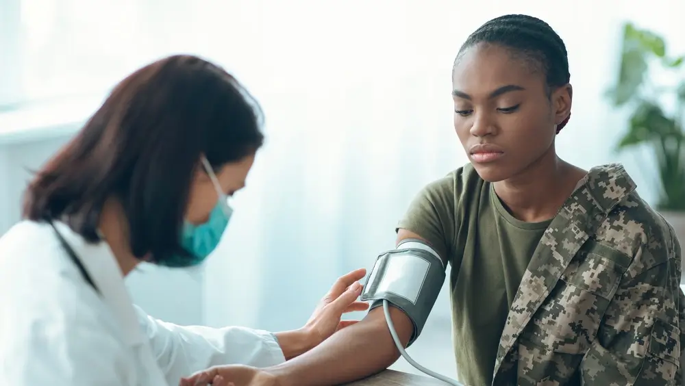 Medico misura la pressione a una candidata in divisa mimetica durante la visita medica militare di controllo.