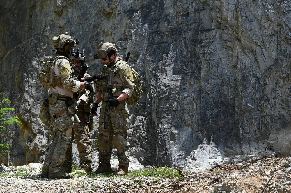 Allievi ufficiali in mimetica durante un'esercitazione militare di addestramento tattico vicino a una parete rocciosa.