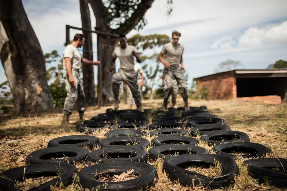Allievi ufficiali impegnati in un'esercitazione militare con pneumatici, indossando anfibi e divisa mimetica.