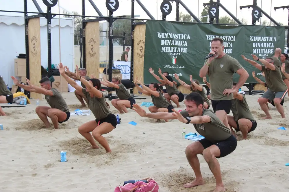 Allievi dell'Esercito impegnati in esercizi di squat sulla sabbia durante una sessione di addestramento militare fisico.