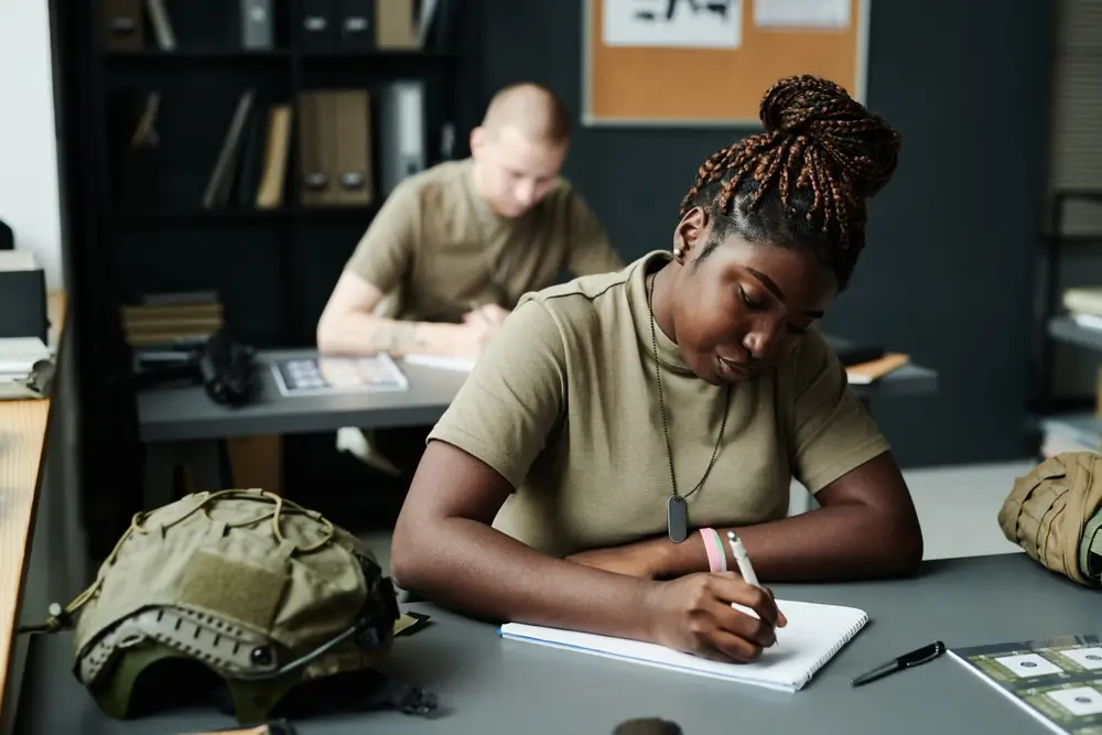 Allieva militare studia e prende appunti in un'aula dell'accademia, con un elmetto poggiato sulla scrivania.